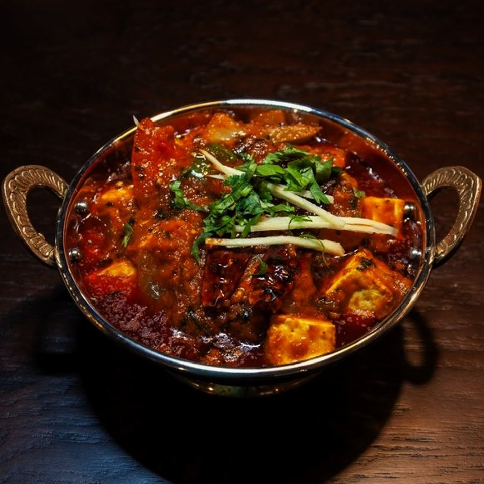 Indian paneer curry with cilantro and ginger in a metal serving bowl on a dark table.