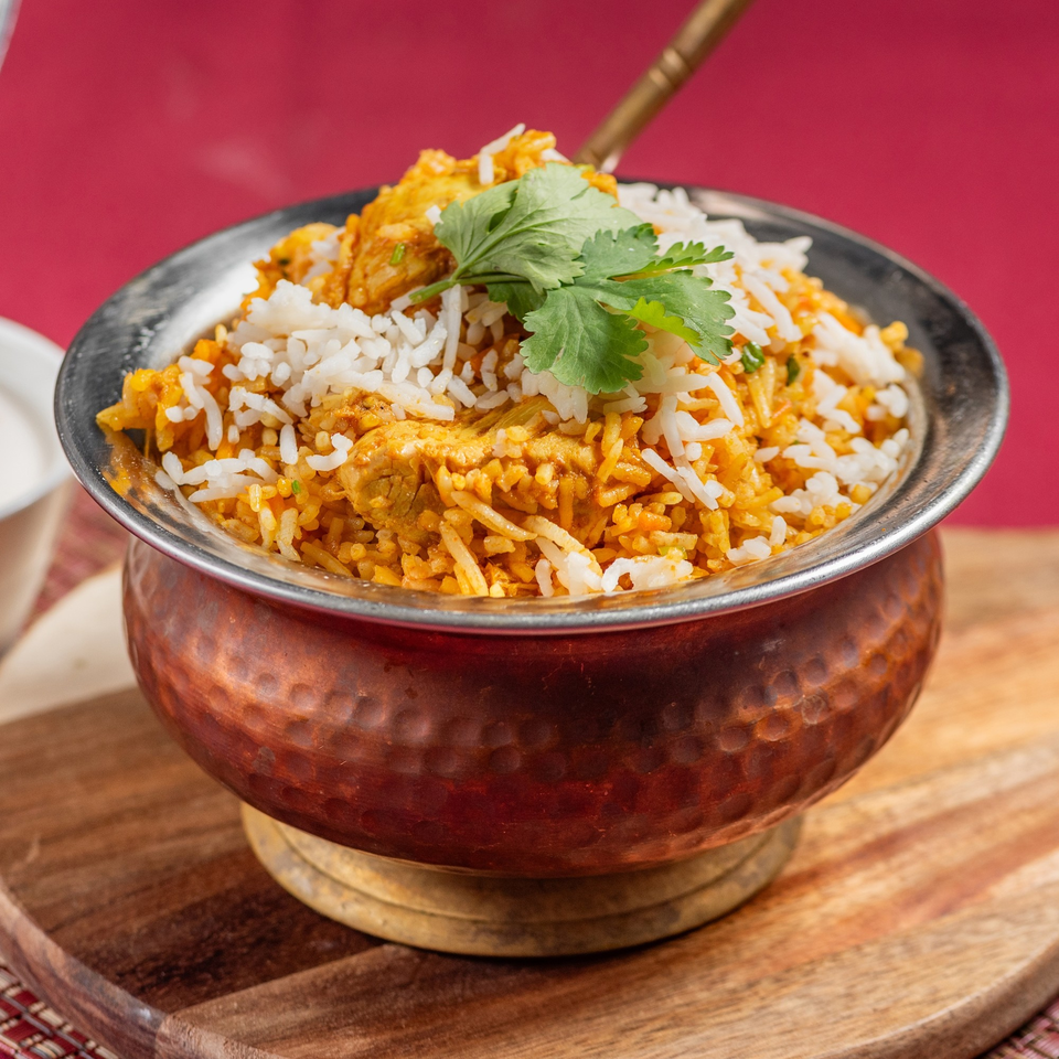 Indian chicken biryani with white rice and cilantro in a copper bowl on a wooden board.