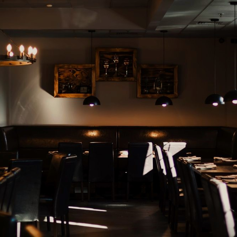Dimly lit Indian restaurant interior with dark booths, tables, and decorative wall art.