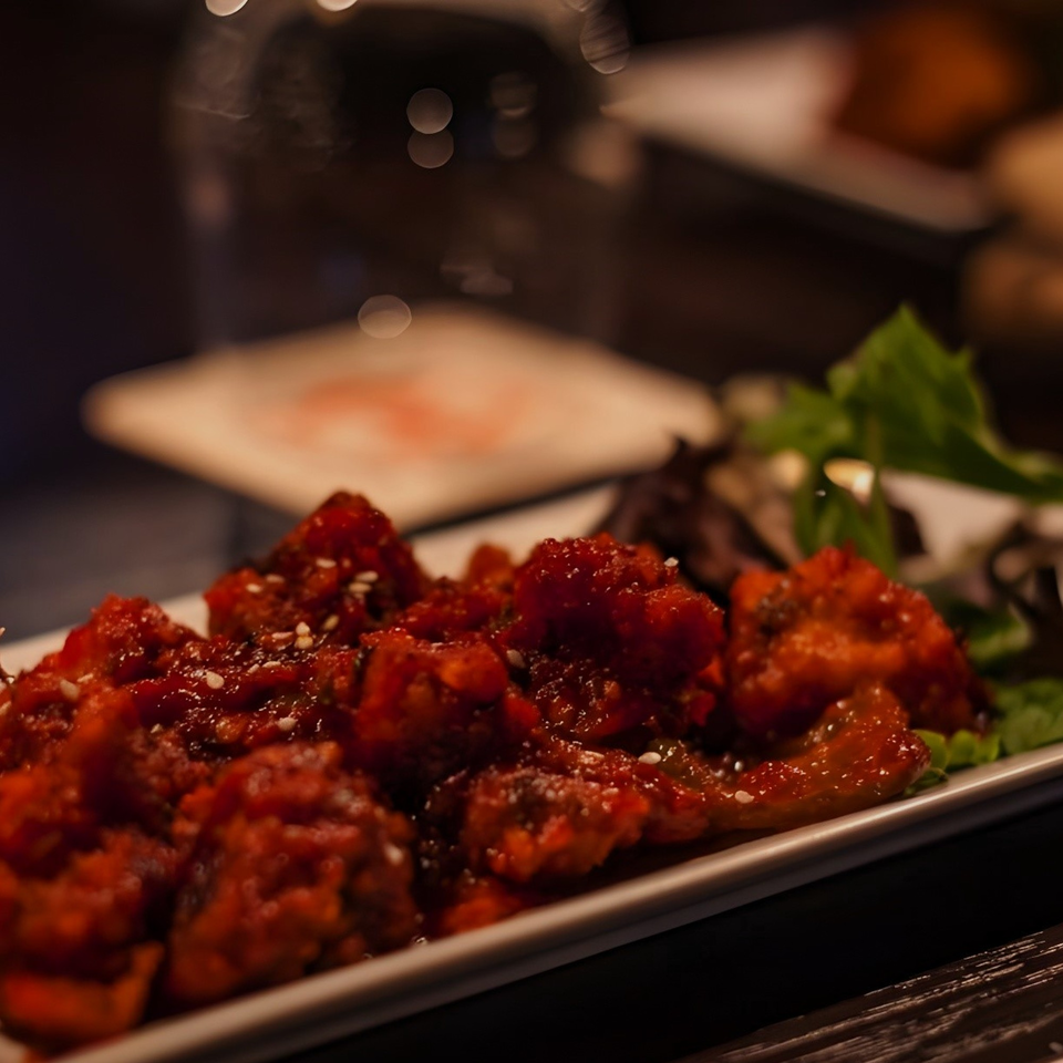 Close-up of Indian chili chicken, garnished with sesame seeds and lettuce, on a white rectangular plate.