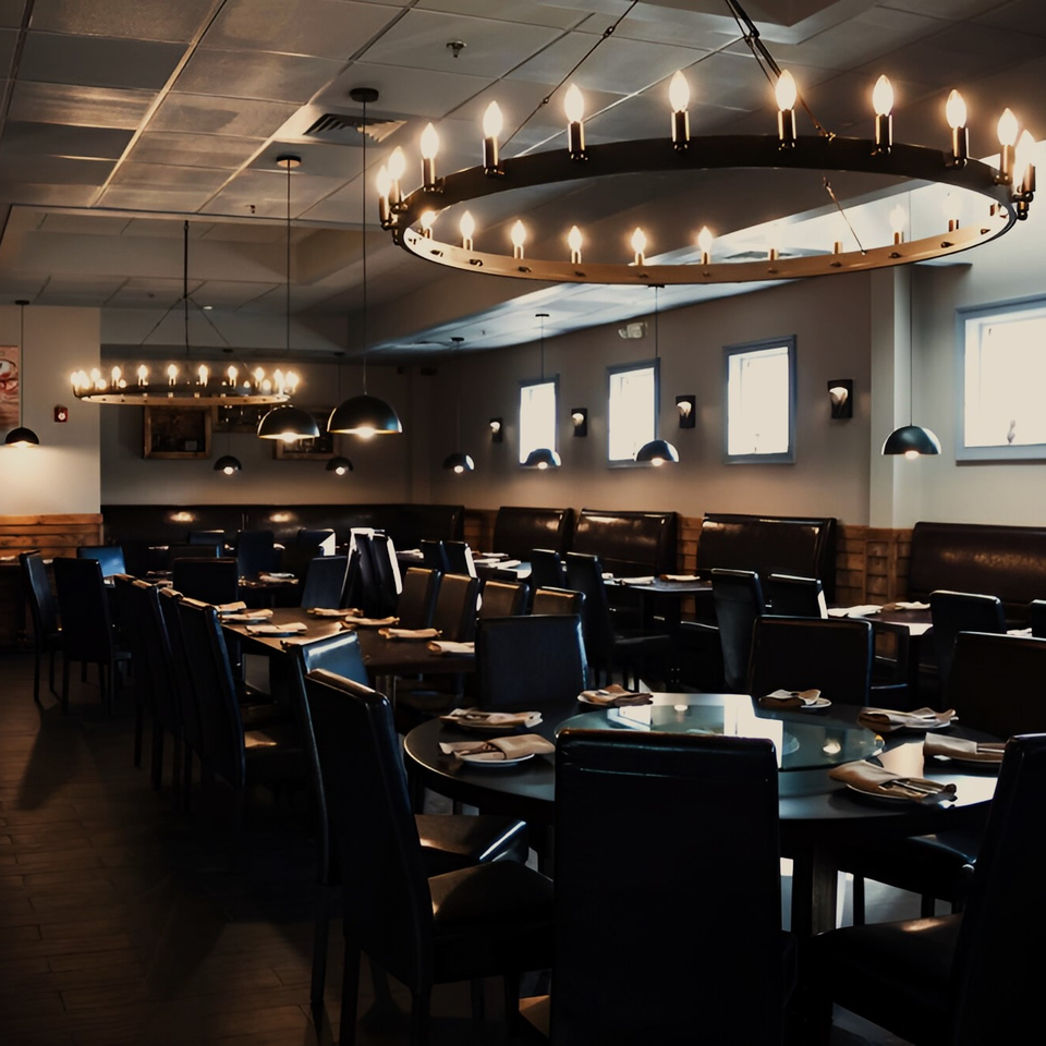 The Naan's dimly lit dining room with dark tables, chairs, and booths, illuminated by chandeliers.